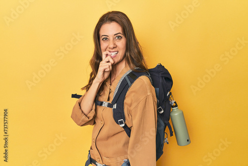 Middle aged woman prepped for hiking, yellow studio shot biting fingernails, nervous and very anxious.
