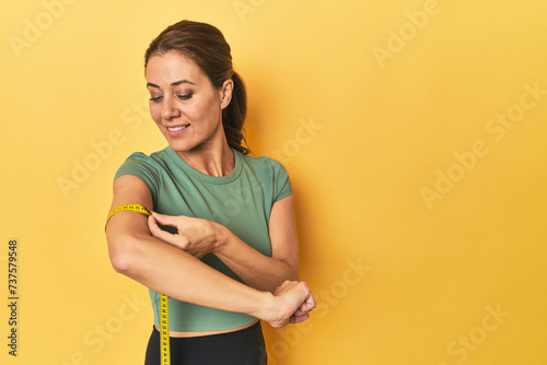 Schilderij op canvas Middle aged woman measuring arm size on a yellow background