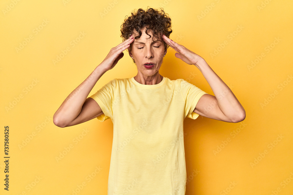 Mid-aged caucasian woman on vibrant yellow touching temples and having headache. Mid-aged caucasian woman on vibrant yellow touching temples and having headache.