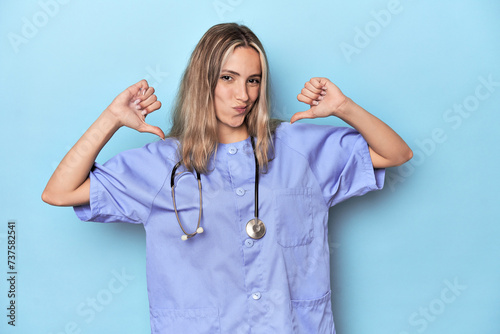 Young caucasian nurse in blue studio feels proud and self confident, example to follow. photo