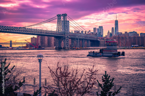 Lower Manhattan Sunset Skyline, Dramatic Saturated Vibrant Purple Clouds, Williamsburg Bridge, Brooklyn Bridge, and Cruising Ferry on the East River in Brooklyn, New York, USA photo