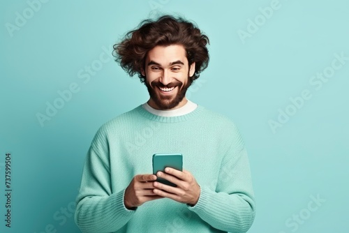 fun young man wear knitted sweater hold in hand use mobile cell phone look aside on workspace isolated on plain pastel light blue cyan background studio portrait - generative ai