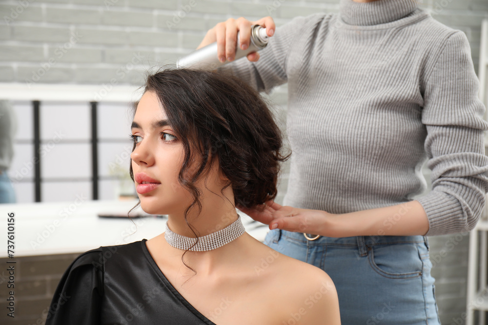 Fototapeta premium Professional hairdresser applying hair spray on young woman's hair in beauty salon
