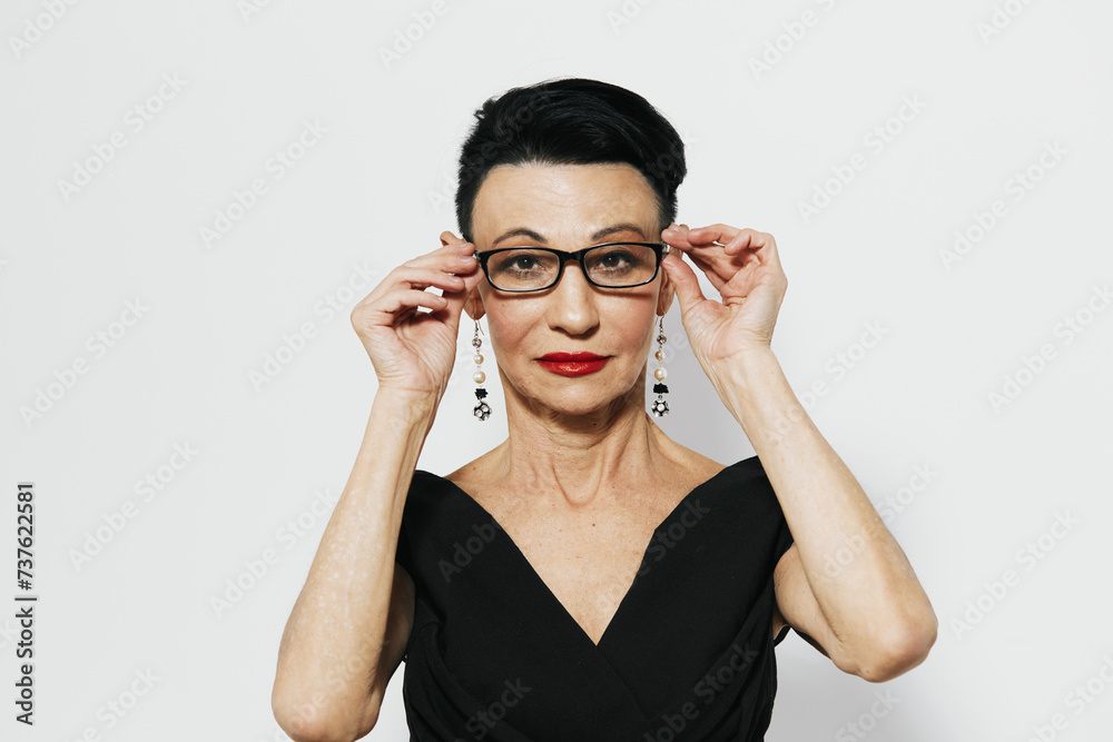 Elegant woman holding eyeglasses up to face in black dress with sophisticated look on white background Elegant woman holding eyeglasses up to face in black dress with sophisticated look on white background