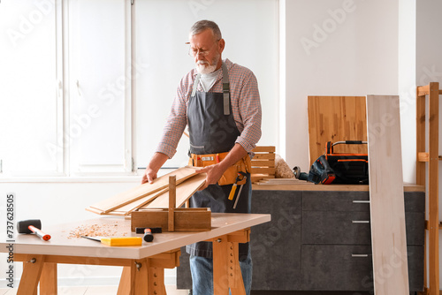 Mature carpenter with wooden planks at table in workshop