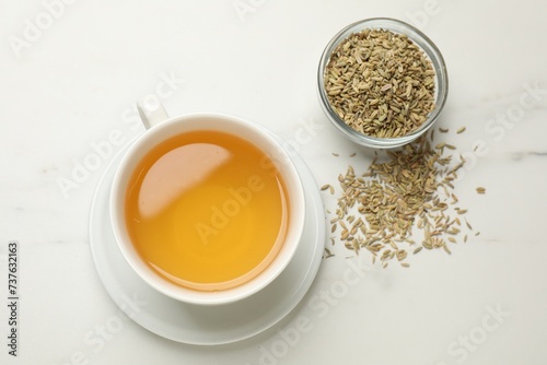 Fennel tea in cup and seeds on white marble table, flat lay
