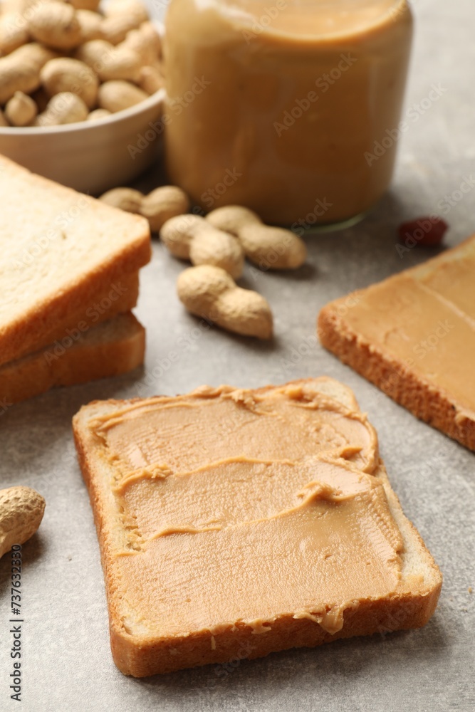 Tasty peanut butter sandwiches and peanuts on gray table, closeup
