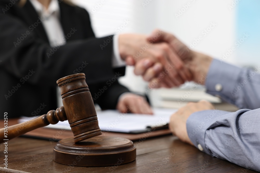 Lawyer shaking hands with client in office, focus on gavel Lawyer shaking hands with client in office, focus on gavel