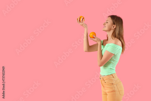 Pretty young woman with oranges on pink background
