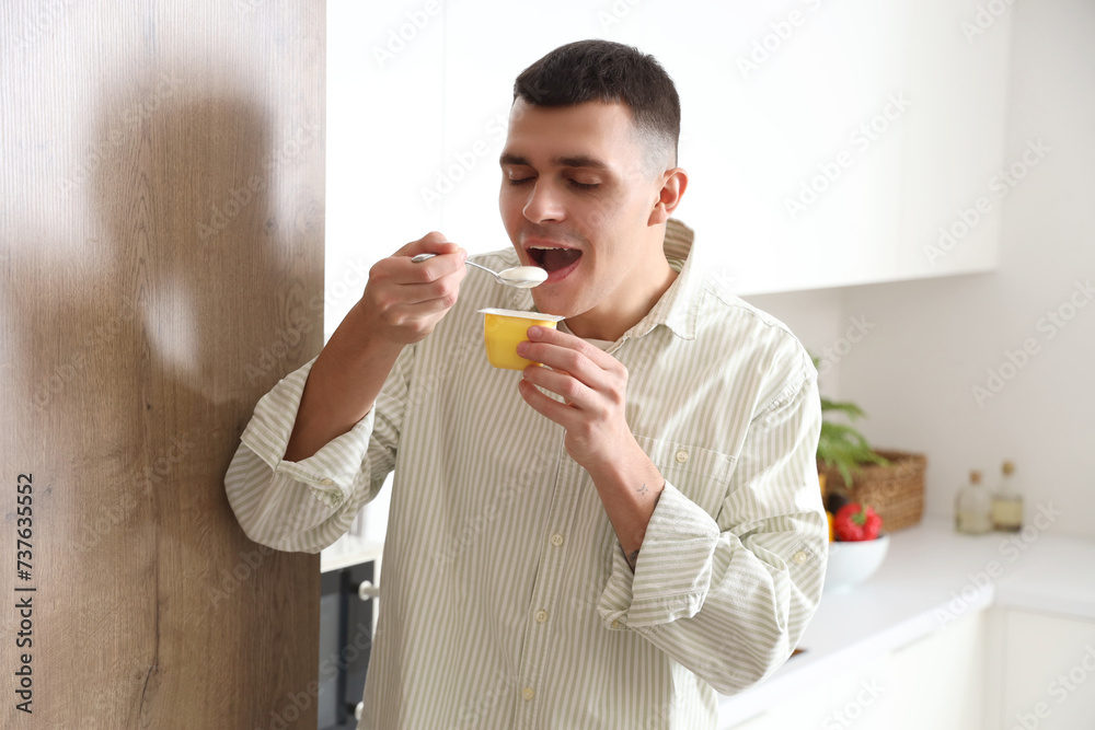 Fototapeta premium Young man eating tasty yogurt in kitchen