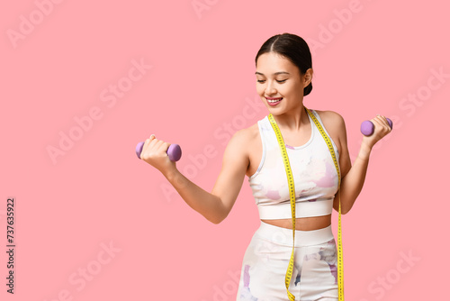 Young woman in sportswear, with dumbbells and measuring tape on pink background. Weight loss concept