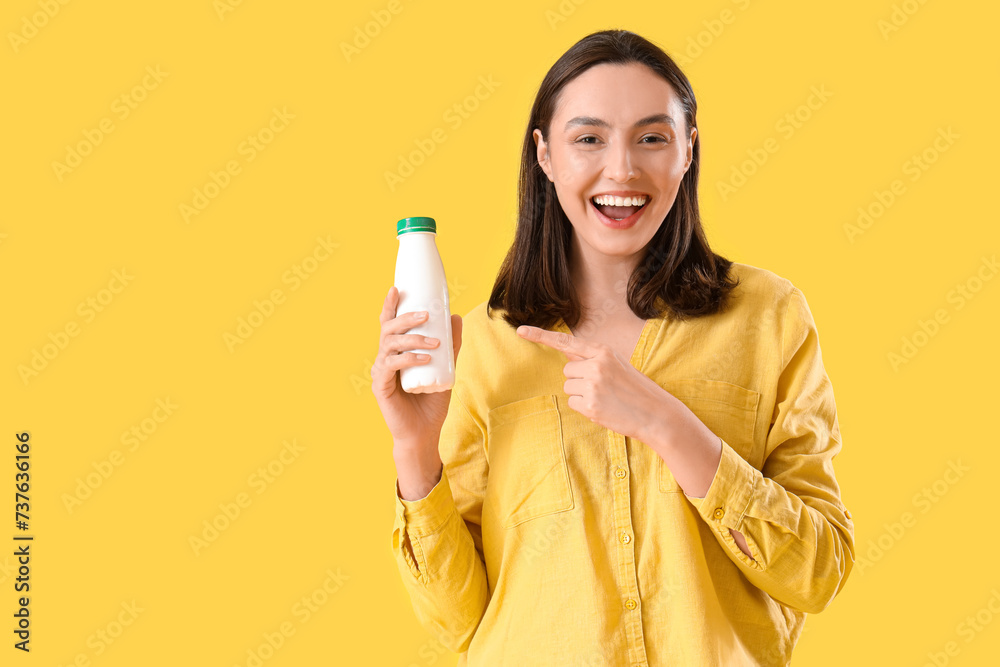 Happy young woman pointing at bottle of tasty yoghurt on yellow background Happy young woman pointing at bottle of tasty yoghurt on yellow background