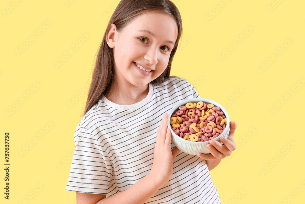 Cute little girl with bowl of cereal rings on yellow background