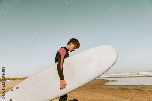 Back view of male surfer in wetsuit with his surfboard entering the sea. Surfing and ocean