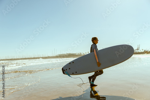 Happy female surfer in wetsuit with his surfboard entering out of sea after surfing on waves