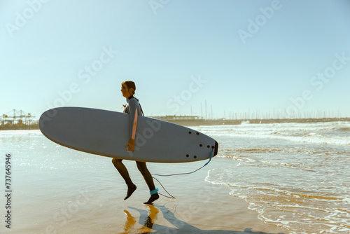 Female surfer in wetsuit with his surfboard entering out of sea after surfing on waves