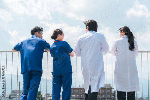 病院の屋上で休憩時間を過ごす男女の医師・医者・看護師・医療従事者・技師の後ろ姿（4人）
 photo