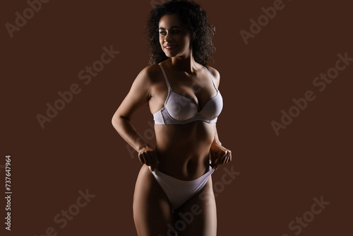 Beautiful young happy African-American woman with stretch marks on her body against beige background