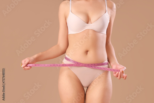 Beautiful young African-American woman with stretch marks on her body and measuring tape against beige background, closeup