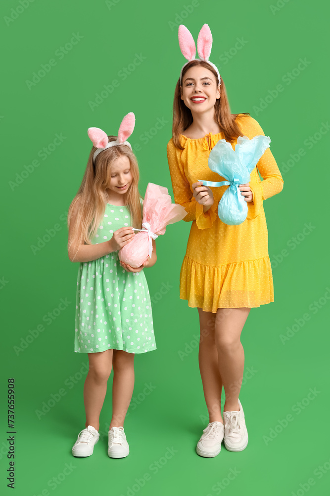 Cute little girl and her mother in bunny ears with Easter gift eggs on green background Cute little girl and her mother in bunny ears with Easter gift eggs on green background