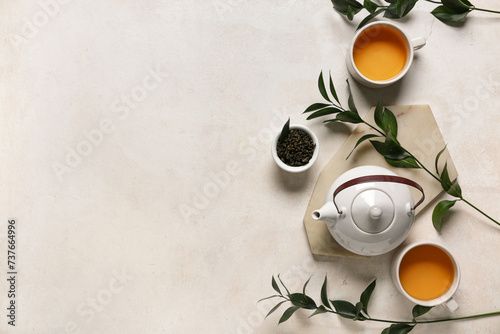 Teapot with cups, bowl of dry tea and leaves on white grunge background