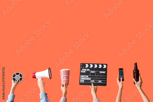 Many hands with bucket of popcorn, movie clapper and beer on orange background photo