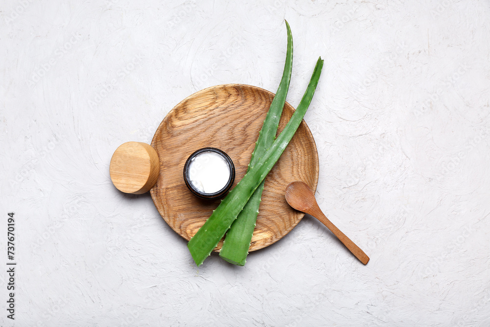 Wooden plate with jar of cosmetic product and aloe vera leaves on grey background