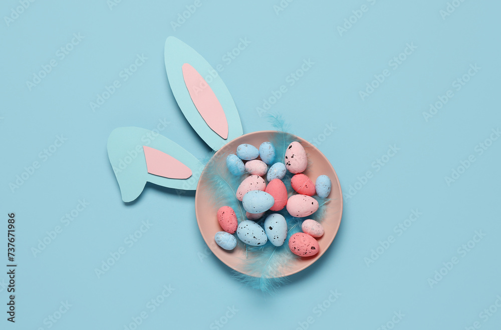 Plate with Easter eggs, feathers and bunny ears on blue background Plate with Easter eggs, feathers and bunny ears on blue background