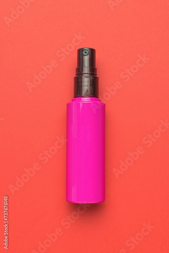 A red bottle with spray on a red background.