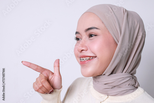 Close-up of Muslim girl with dental braces pointing finger with happy expression, side view