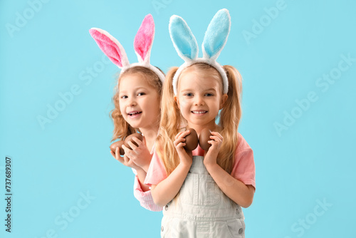 Cute little girls in bunny ears with chocolate Easter eggs on blue background