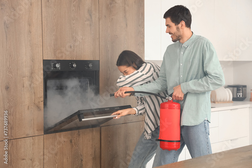 Bilde på lerret Young couple extinguishing fire in oven at home