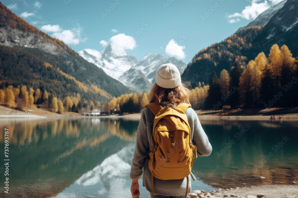 Young Woman with Backpack Standing on Mountain Peak, Admiring Winter Landscape and Reflective Lake on Sunny Day, Hiking Adventure