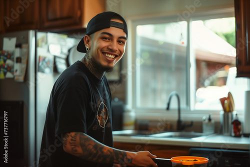 hispanic young man cooking in kitchen holding a strainer streetwear at home latino guy bearded with a cap backwards smiling happy joyful sink fridge cheerful large black tshirt homemade food window