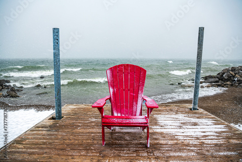 Photography seat in the storm: a red beach chair on a wooden dock facing the camera with a w