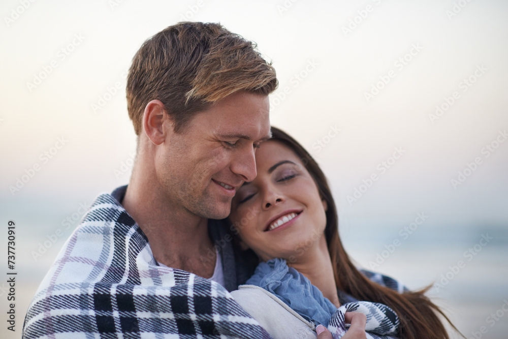 Fototapeta premium Couple, hug and happy at beach with blanket for vacation, love and care on date at sunset by ocean. Man, woman and embrace with smile, bonding and happy for memory on holiday by sea in Australia