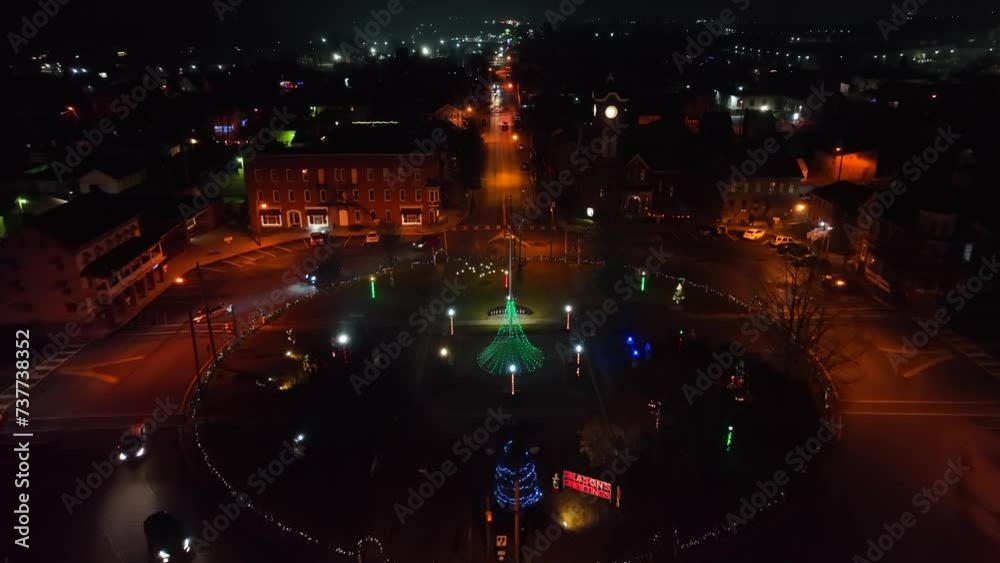 Aerial night view of a roundabout with a lit Christmas tree and colorful festive lights in an American town.