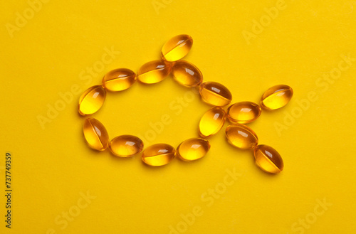 Fish oil capsules in the shape of a fish on yellow background