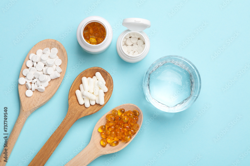 Pills in wooden spoons and glass of water on blue background Pills in wooden spoons and glass of water on blue background