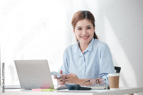Cheerful Successful Asian Business woman using calculator and laptop for doing math finance on an office desk, tax, report, accounting, statistics, and analytical research concept 
