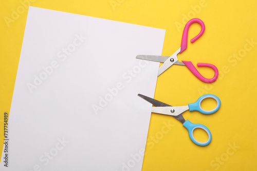Scissors for creativity cut a white sheet of paper on a yellow background