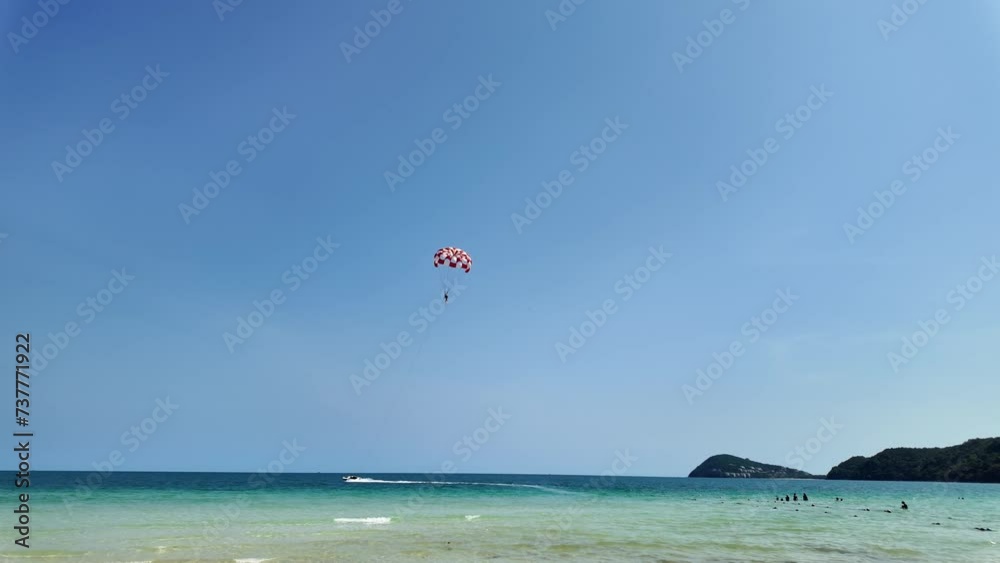 Tropical beach scene with vibrant blue skies, crystal-clear water, and a person parasailing with a red and white parachute, evoking a sense of adventure and leisure in summer holidays Tropical beach scene with vibrant blue skies, crystal-clear water, and a person parasailing with a red and white parachute, evoking a sense of adventure and leisure in summer holidays