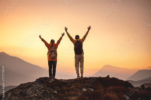 Two hikers are standing in winner pose at mountain top