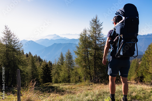 Man with baby carrier looking at magical mountain peaks of Karawanks and Julian Alps seen from Goldeck, Latschur group, Gailtal Alps, Carintha, Austria. Mystical atmosphere in Austrian Alps in summer photo