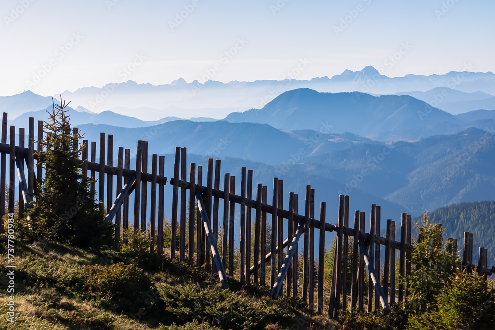Wooden fence with scenic view of magical mountain peaks of Karawanks and Julian Alps seen from Goldeck, Latschur group, Gailtal Alps, Carinthia, Austria. Mystical atmosphere. Austrian Alps in summer