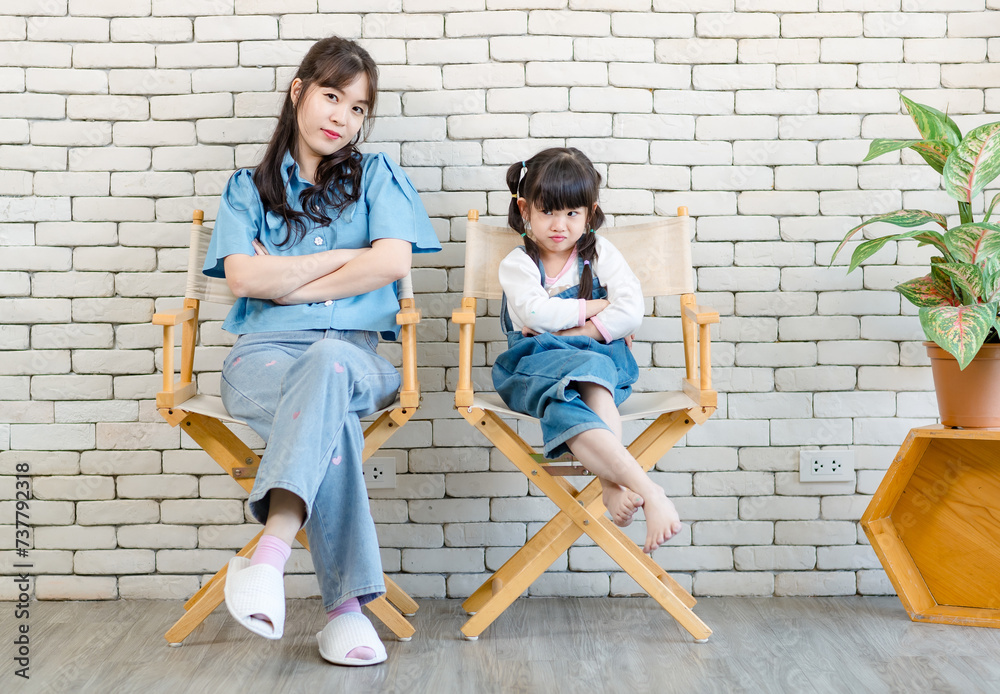 Asian beautiful young mother cute daughter little girl posing cross arm and sitting on chair, white brick wall background studio portrait Mother's Day love family parenthood childhood concept. Asian beautiful young mother cute daughter little girl posing cross arm and sitting on chair, white brick wall background studio portrait Mother's Day love family parenthood childhood concept.