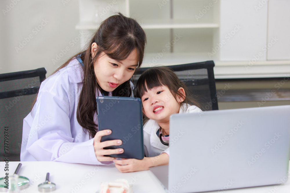 Asian woman scientist and little children girl reading laptop and tablet computer for data learning at chemical laboratory study room. Education research and development concept learning for kids. Asian woman scientist and little children girl reading laptop and tablet computer for data learning at chemical laboratory study room. Education research and development concept learning for kids.