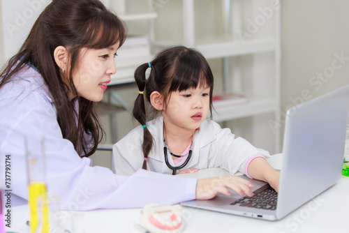 Asian woman teacher and little children girl reading laptop computer for data learning science at chemical laboratory study room. Education research and development concept learning for kids.