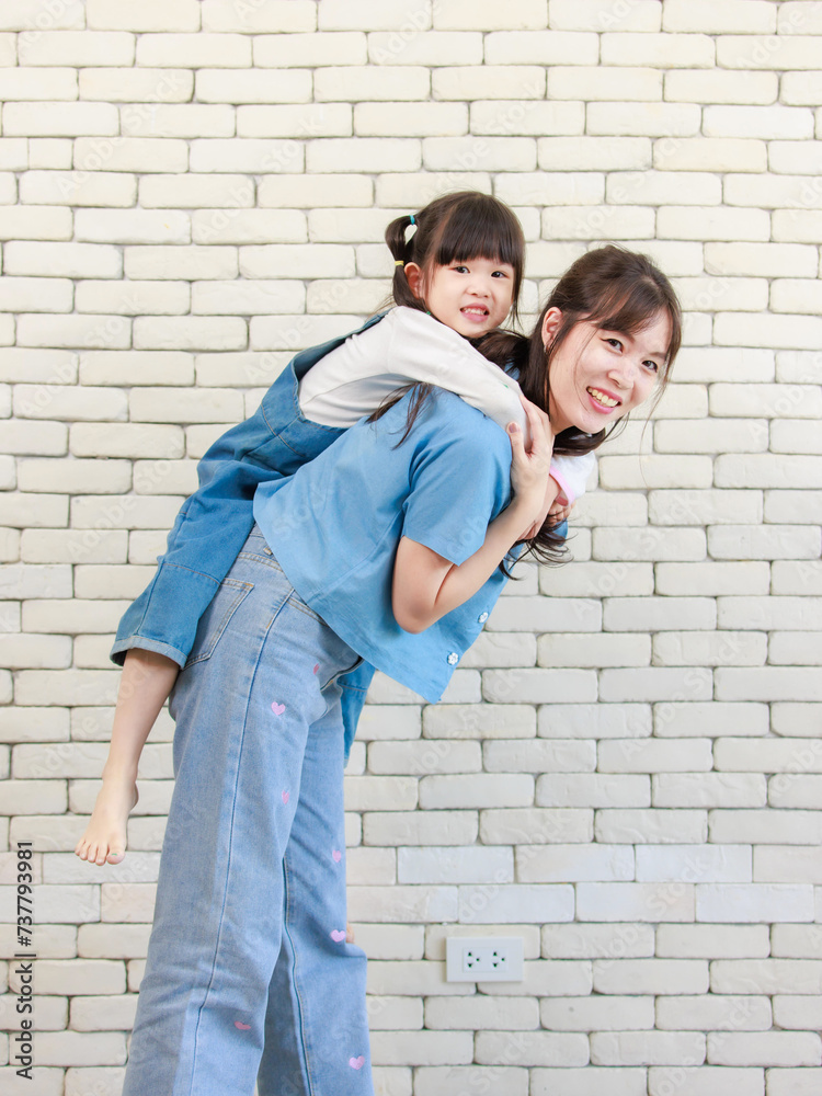 Happy asian beautiful young mother holding cute daughter little girl smiling posing on white brick wall background studio portrait Mother's Day love family parenthood childhood concept. Happy asian beautiful young mother holding cute daughter little girl smiling posing on white brick wall background studio portrait Mother's Day love family parenthood childhood concept.