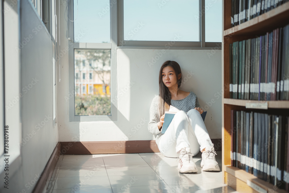 Young asian female college student sitting on floor in library, reading book. Young asian female college student sitting on floor in library, reading book.